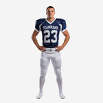 American football uniform packages in navy and white - front view showing team name arc, front number 23, and white V-neck collar on sublimated jersey with matching white pants and navy side stripe