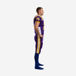 Side profile of purple and gold school football uniform showing white side panel on the jersey and gold-and-white double leg stripe on matching pants