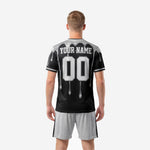 Close-up detail of black and white soccer uniform jersey showing silver metallic drip columns and crew neck contrast trim