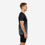 Left side view of black-to-charcoal sublimated mens soccer training jersey showing athletic cut and white sleeve cuff trim