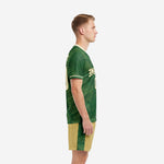Green soccer uniform kit left side view showing cream V-neck trim, sleeve cuff detail, and Vegas Gold shorts with fern stripe