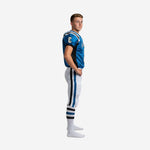 Side view of blue and white youth football uniforms showing black raglan sleeve panel, white pant with 3-stripe blue and black side panel running from hip to cuff and lace-tie belt area