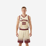Front view of cream and maroon youth basketball uniform sets with halftone dot fade pattern on jersey hem and shorts legs, maroon V-neck binding and arced team name