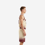 Side view of cream and maroon youth basketball uniform sets showing maroon elastic waistband, athletic cut jersey, and halftone dot fade rising from shorts hem