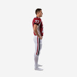 Side view of crimson and white custom american football kit showing white curved shoulder panel, black cuff binding, and crimson-black double leg stripe on white pants