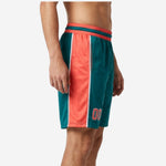 Side view of teal custom basketball shorts for teams showing full-length coral-orange outer panel with white stripe edges and two-tone waistband detail