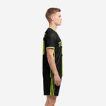 Custom black soccer team uniform set with lime green side stripe shorts, left side view on male model