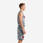 Side view of grey digital camo basketball uniform set showing V-neck binding, armhole trim, and camo shorts with red player number on leg