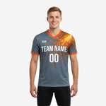 Custom grey soccer training jersey with orange V-neck collar and spark-burst sublimated shoulder print, front view on male model