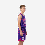 Side view of purple and pink custom kids basketball uniforms showing V-neck binding, claw-slash graphic on jersey and shorts, pink hem trim with side split
