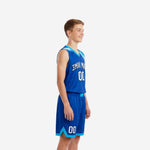 Front view of custom kids basketball uniforms in royal blue with cyan V-neck binding gradient shoulder panel and white arced team name lettering
