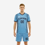 Custom light blue soccer uniform front view showing navy V-neck collar, radiating stripe panels, and matching shorts on adult male model