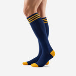 Over the calf custom gold soccer socks in Navy Blue with triple gold cuff stripes, angled side view showing full length