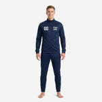 Adult male wearing a custom navy soccer tracksuit with hex dot pattern, stand collar full zip jacket and tapered pants, front view showing chest number and team logo print