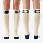Full length pair of custom navy and white soccer socks laid flat showing cream ivory body from ribbed cuff to reinforced navy toe box
