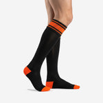 Custom orange and black soccer socks side view displaying ribbed elastic cuff stripe and orange contrast heel panel on men's over the calf sock