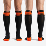Men's custom orange and black soccer socks full-length profile view showing over the calf fit with orange stripe cuff and black body
