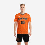 Custom orange soccer uniform front view showing geometric grid jersey and black shorts on adult male model