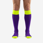 Custom purple and gold soccer socks with neon yellow ribbed cuff and reinforced toe, front view on adult male