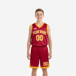 Custom red youth basketball uniforms in crimson and gold showing arced team name, front number, and chevron gold hem trim on matching shorts - front and back view
