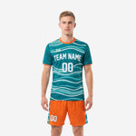 Custom soccer uniform kits in teal wave print jersey and orange shorts, front view on adult male model