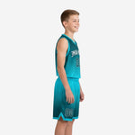 Front view of custom teal youth basketball uniform with arced team name, front number, and dark teal hex-pattern gradient on jersey and shorts