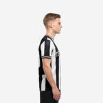 Custom team soccer jersey black and white stripe design, left side view showing athletic cut and sleeve cuff trim on male model
