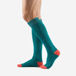 Custom teal knee-high soccer socks with coral heel and geometric cuff band, angled side view showing athletic cut construction
