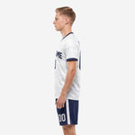 Custom white soccer uniform set with navy blue V-neck trim and matching shorts, right side view on male model