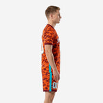 Full print custom orange soccer uniform in Athletic Orange and Maroon camo with teal stripe, side view on male model