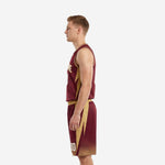 Side view of custom maroon and gold basketball uniforms showing gold lightning bolt panel running from jersey side through the outer shorts leg