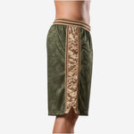 Side view of custom green basketball shorts showing wide tan and brown digital camo side panel with tan trim lines running from waistband to hem split