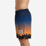 Custom team basketball shorts showing navy-to-orange gradient design with city skyline silhouette across the hem, side angle on adult male model