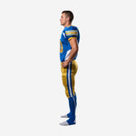 Blue and gold football uniform side view from right showing V-neck collar with gold trim, athletic torso cut, and gold pants lace-up belt area