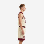 Side view of cream and maroon men's basketball uniform set showing maroon armhole binding on sleeveless jersey and maroon hem band on shorts