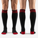 Full-length view of custom red and black over-the-calf soccer socks with red toe contrast on male model