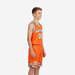 Side view of orange and gray sublimated youth basketball jersey and shorts showing splash splatter pattern across left shoulder and shorts hem trim