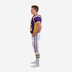 Left side view of purple and gold youth football uniform showing gold jersey side panel and white pants with purple gold outer leg stripe