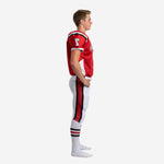 Side view of red and white youth football uniform set showing black shoulder panel accent, white jersey side insert, and full-length red and black pant stripe panel