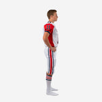 Side view of custom red and white youth football uniforms showing red shoulder panel with back number, set-in sleeve with navy cuff trim, and white pants with full-length red and navy outer leg stripe