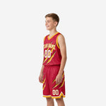 Youth basketball uniform in crimson red with diagonal gold claw marks, left side view showing armhole binding and drawcord waistband