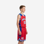 Side view of red and blue youth basketball uniform set showing angular royal blue panel on jersey shoulder and matching geometric insert on shorts with white hem stripe