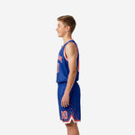 Side view of royal blue youth basketball jersey and shorts set showing red orange dot-burst side panel pattern and white armhole binding detail