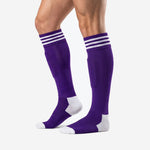 Adult male wearing custom purple soccer socks with white stripe cuff band and white reinforced toe, angled view