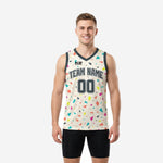 Front view of sublimated basketball jersey designs in cream with scattered multicolor geometric shapes and dark charcoal V-neck trim, team name and number 00 on chest