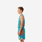 Side view of teal youth basketball uniform set showing orange geometric shard pattern extending across jersey sides and shorts panels