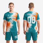 Front view of men's vivid teal custom soccer uniform kit with orange splash design and crew neck trim