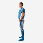 Side view of sublimated light blue and white football uniform showing white torso side panel meeting the jersey body and full-length white pants with navy triple leg stripe