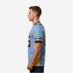 Side view of sublimated light blue football jersey showing gold side panel running from underarm to hem and navy cuff detail