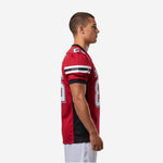 Side view of red and black custom youth football jersey showing black side panel, sleeve stripe detail, and straight hem on a male model